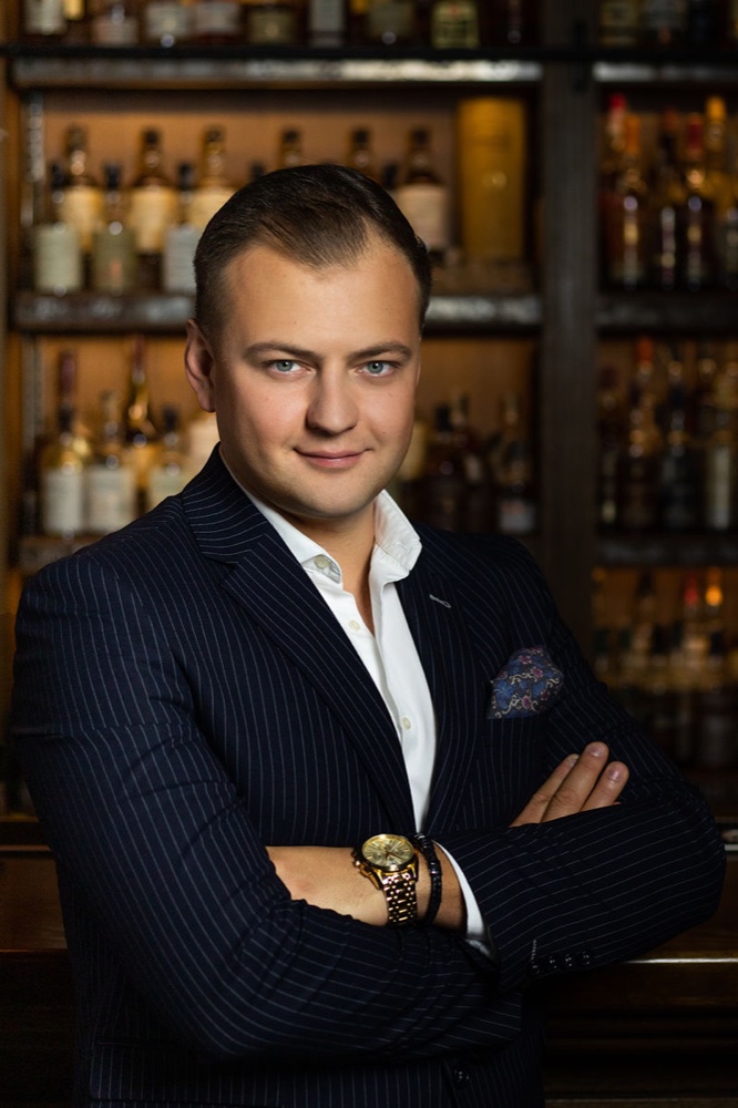 Mężczyzna w garniturze w prążki na tle eleganckiego baru.